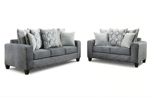 Juego de sala moderno compuesto por sofá y loveseat tapizados en tela gris, con cojines decorativos en patrones geométricos y rayas en tonos gris y blanco, sobre fondo blanco.
