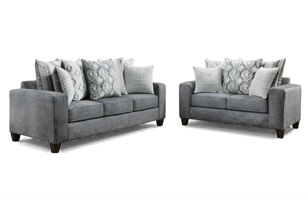 Juego de sala moderno compuesto por sofá y loveseat tapizados en tela gris, con cojines decorativos en patrones geométricos y rayas en tonos gris y blanco, sobre fondo blanco.