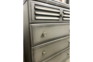 Vista cercana de chest de color gris con cinco gavetas con manijas redondas sobre un fondo blanco. 