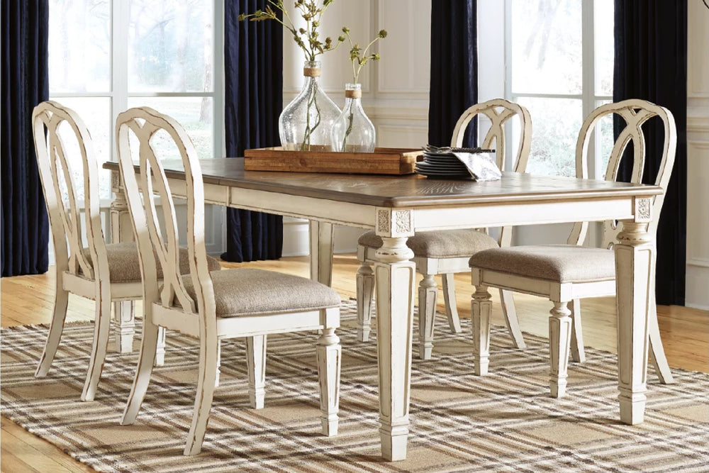 Mesa rectangular con tope de madera marrón y patas blancas decapadas, rodeada de 4 sillas tapizadas en tono crema con respaldos curvos, sobre alfombra de rayas.