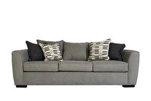 Sofá moderno de tres plazas en tela gris clara, con cojines de asiento acolchados y almohadas decorativas en tonos negro y blanco con patrón geométrico, sobre fondo blanco.