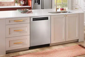 Un lavaplatos empotrado de acero inoxidable instalado bajo una encimera blanca de una isla de cocina con armarios color crema y tiradores dorados.