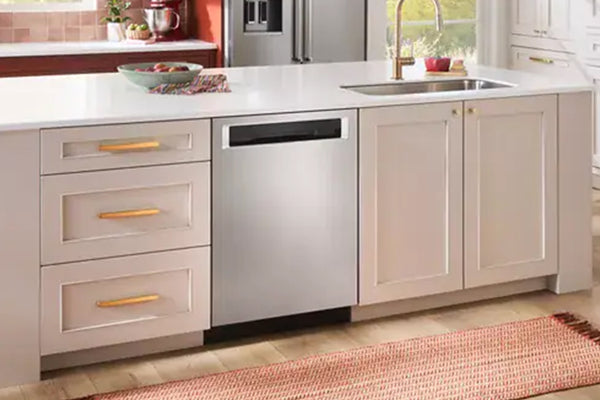 Un lavaplatos empotrado de acero inoxidable instalado bajo una encimera blanca de una isla de cocina con armarios color crema y tiradores dorados.