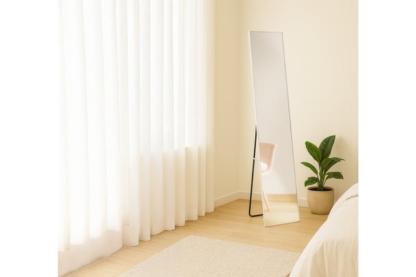 Dormitorio moderno con espejo de pie, planta y cortinas de colores claros.