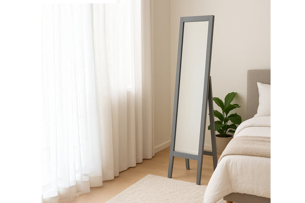 Espejo de cuerpo entero apoyado contra una pared en un dormitorio con cortinas y una cama.