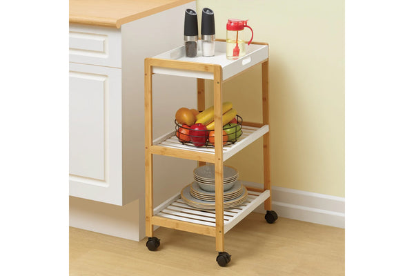 Carrito de cocina de madera con fruta y platos sobre un suelo de madera clara.