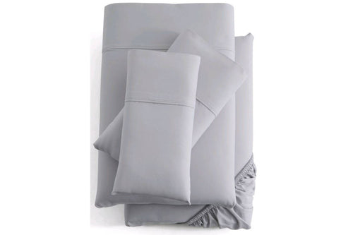 Juego de cama de color gris que incluye un edredón, dos almohadas y una sábana ajustable sobre fondo blanco.