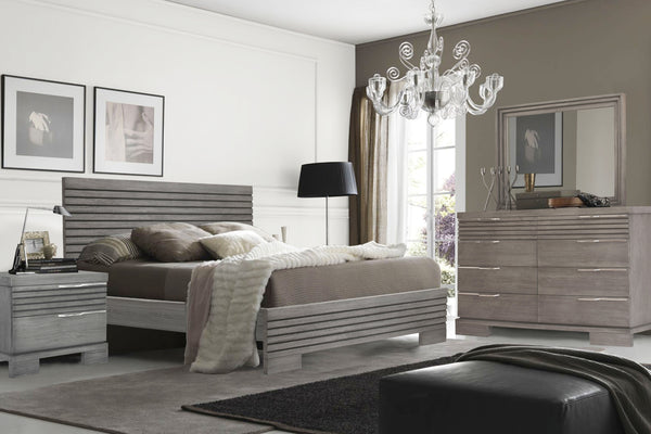 Conjunto de dormitorio gris de madera que incluye una cama, un gavetero con espejo y una mesa de noche en una habitación con una ventana en una esquina.
