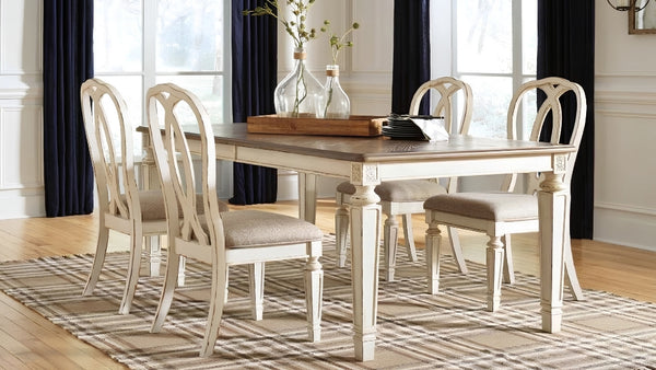 Mesa rectangular con tapa de madera marrón rústica y patas blancas decapadas, rodeada de 4 sillas tapizadas en tono crema con respaldos curvos, sobre alfombra de rayas.