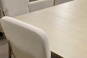 Primer plano de silla tapizada en tela color marfil junto a una mesa de comedor en acabado madera clara. La imagen resalta la textura suave del tapizado y la superficie de la mesa, destacando su diseño moderno y elegante.