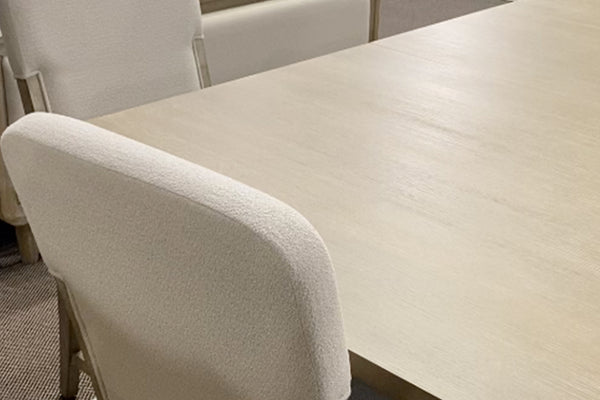 Primer plano de silla tapizada en tela color marfil junto a una mesa de comedor en acabado madera clara. La imagen resalta la textura suave del tapizado y la superficie de la mesa, destacando su diseño moderno y elegante.