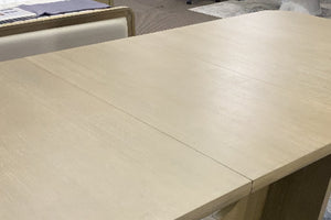 Primer plano de mesa de comedor rectangular en acabado madera clara con superficie lisa y veta sutil visible. La imagen destaca el amplio espacio de uso, las líneas limpias y el diseño contemporáneo en tonos neutros.