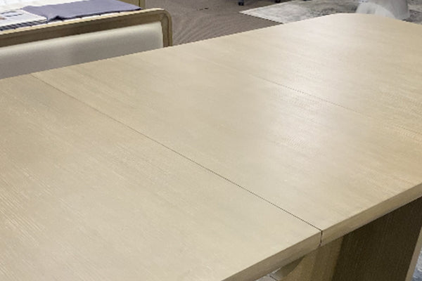 Primer plano de mesa de comedor rectangular en acabado madera clara con superficie lisa y veta sutil visible. La imagen destaca el amplio espacio de uso, las líneas limpias y el diseño contemporáneo en tonos neutros.