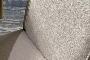 Primer plano de silla de comedor tapizada en tela color marfil con textura bouclé, mostrando el respaldo y asiento acolchados. La imagen resalta el tejido suave, los acabados y el diseño elegante de estilo contemporáneo.