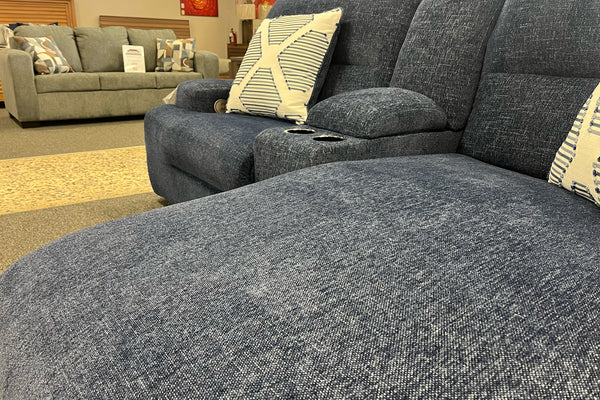 Sofá seccional gris con cojines estampados en un entorno de exposición.