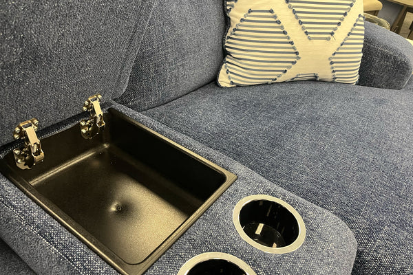 Sofá gris con lavabo incorporado y portavasos. En un entorno de exposición.