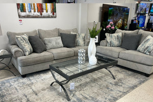 Sofá y loveseat gris con cojines decorativos en una sala de exposición.