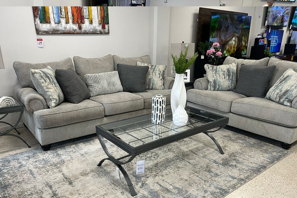 Sofá y loveseat gris con cojines decorativos en una sala de exposición.