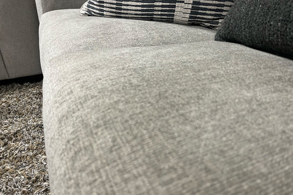 Sofá gris texturizado con cojín a rayas sobre una alfombra.