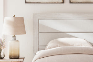 Cama cuidadosamente hecha con ropa de cama blanca y una lámpara en la mesita de noche en un dormitorio.