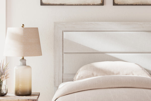 Cama cuidadosamente hecha con ropa de cama blanca y una lámpara en la mesita de noche en un dormitorio.