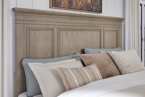 Cabecera de cama matrimonial en madera clara con paneles decorativos, acompañada de almohadas en tonos neutros y una manta, ubicada en una habitación luminosa con pared clara y cuadro decorativo encima.