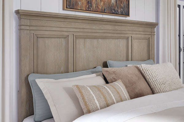 Cabecera de cama matrimonial en madera clara con paneles decorativos, acompañada de almohadas en tonos neutros y una manta, ubicada en una habitación luminosa con pared clara y cuadro decorativo encima.