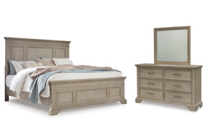 Juego de dormitorio de estilo clásico en madera clara que incluye cama matrimonial con cabecera y pie con paneles decorativos, y gavetero con seis gavetas y tiradores metálicos, acompañado de espejo rectangular a juego, todo sobre fondo blanco.