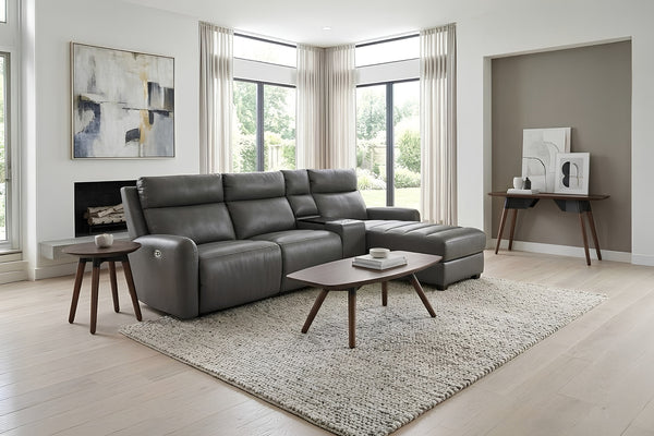Un moderno sofá seccional de cuero gris con un chaise longue y reclinables integrados, en una sala contemporánea y luminosa con una alfombra texturizada clara, una mesa de centro y mesas auxiliares de madera.