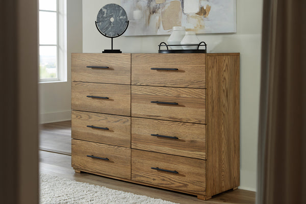 Gavetero de madera de 7 gavetas con acabado en roble cálido y tiradores de metal negro, ambientado en un dormitorio y decorado con objetos ornamentales en la parte superior.