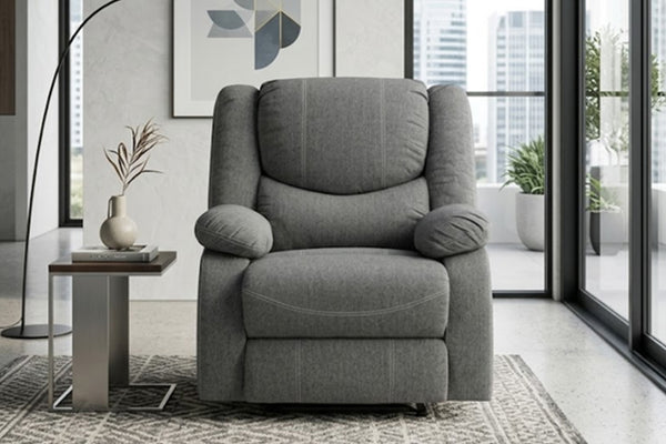 Una butaca reclinable moderna tapizada en gris, ubicado en una sala de estar contemporánea con una mesa auxiliar, una lámpara de pie y grandes ventanales con vistas al horizonte de la ciudad.