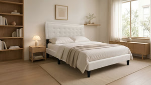 Cama Queen Kai con tapizado en tela color crema, cabecera capitonée de diseño rectangular y patas negras elevadas, en un dormitorio moderno con estantería y luz cálida.