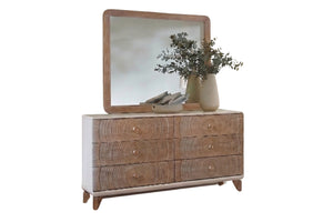 Un gavetero de madera de estilo moderno de mediados de siglo con seis gavetas que presentan vetas de madera muy marcadas y pequeños tiradores redondos, rematada con un espejo a juego con marco de madera. La cómoda está decorada con un jarrón con plantas sobre un fondo blanco liso