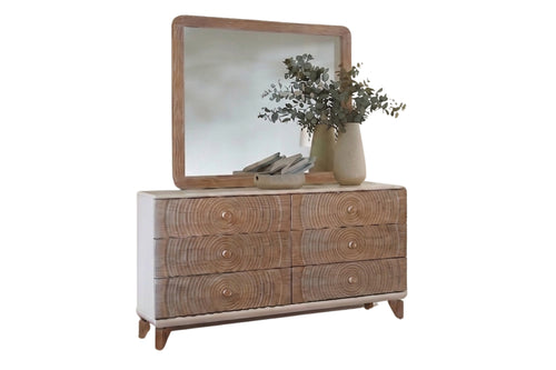 Un gavetero de madera de estilo moderno de mediados de siglo con seis gavetas que presentan vetas de madera muy marcadas y pequeños tiradores redondos, rematada con un espejo a juego con marco de madera. La cómoda está decorada con un jarrón con plantas sobre un fondo blanco liso