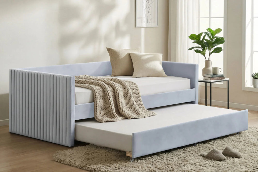 Un daybed tapizado con un panel lateral plisado y una cama nido extensible extraíble, decorado con cojines en tono beige y una manta tejida en color crema en una habitación luminosa y moderna.