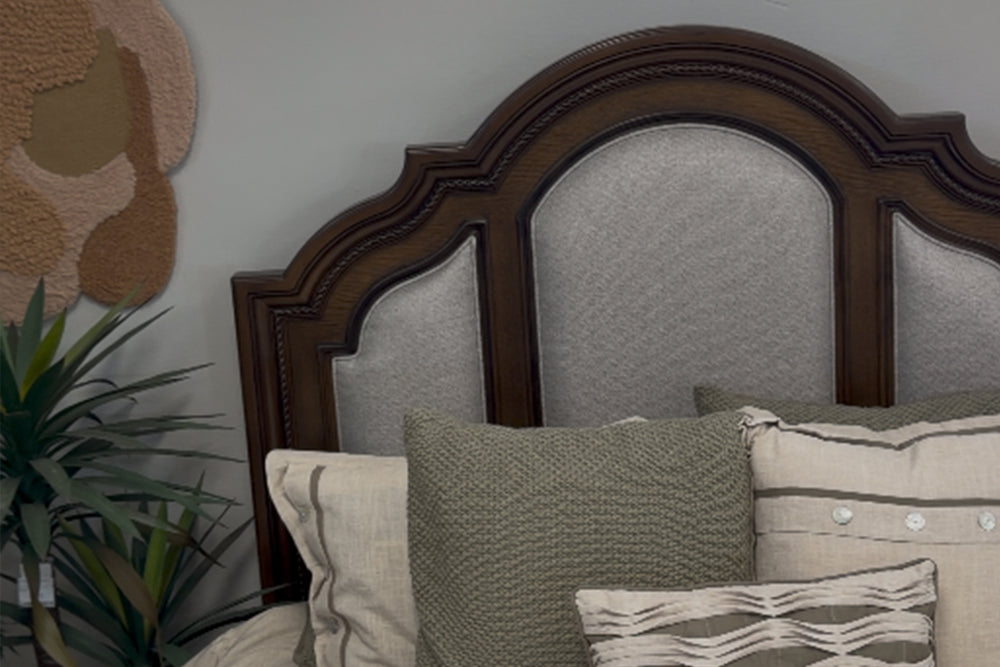 Conjunto de muebles de dormitorio de madera color marrón oscuro, compuesto por cama, gavetero con espejo y mesita de noche, en una habitación con grandes ventanas.