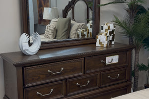 Gavetero hecho de madera marrón oscuro con espejo y con objetos decorativos. 