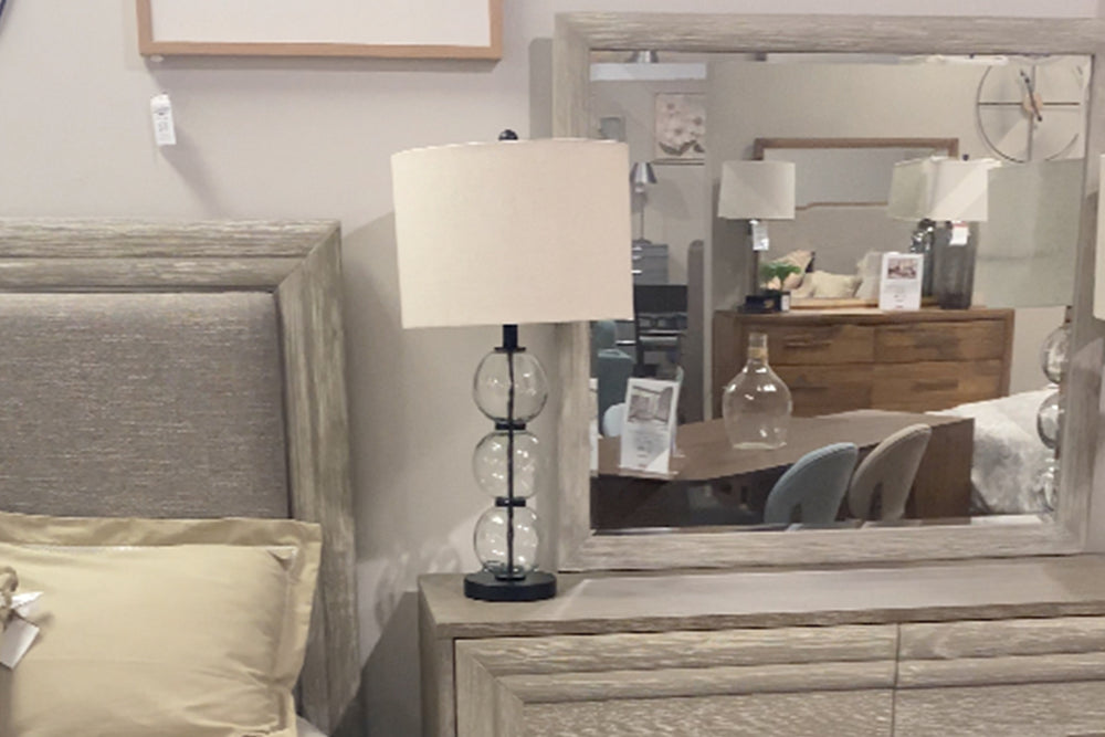 Cama de madera gris en una habitación con chest, gavetero con espejo y mesa de noche. 
