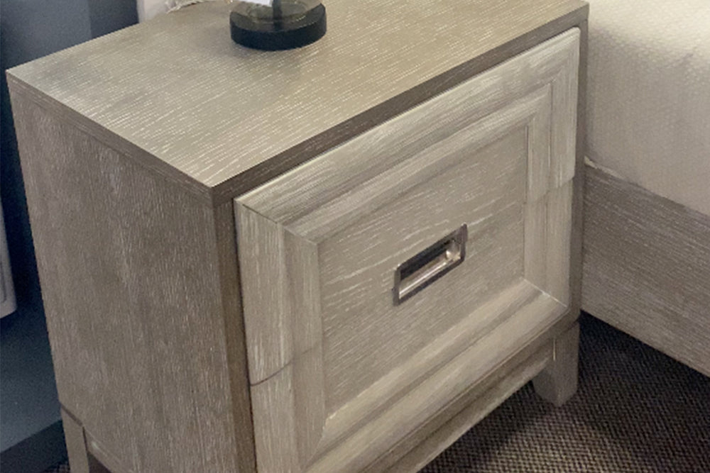 Mesa de noche de dos gavetas gris con objetos decorativos. 