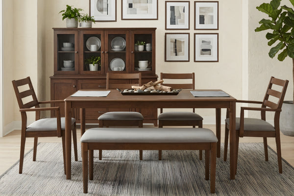 Mesa rectangular de color marrón oscuro con cuatro sillas con acolchado gris y con bench. En una habitación decorada.