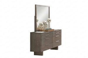 Gavetero de color gris con ocho gavetas y con manijas plateadas horizontales, objetos decorativos encima de tope de gavetero y todo sobre un fondo blanco. 