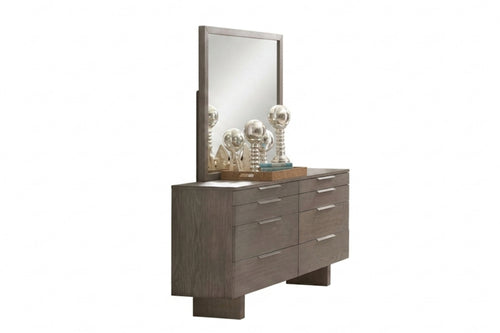 Gavetero de color gris con ocho gavetas y con manijas plateadas horizontales, objetos decorativos encima de tope de gavetero y todo sobre un fondo blanco. 