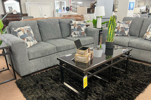 Sofá y loveseat gris con cojines decorativos en un entorno de exposición.