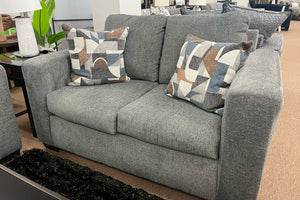Loveseat gris con cojines estampados en un ambiente de habitación.