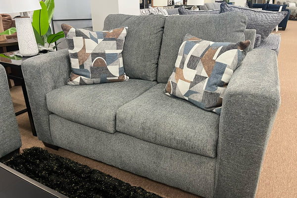 Loveseat gris con cojines estampados en un ambiente de habitación.