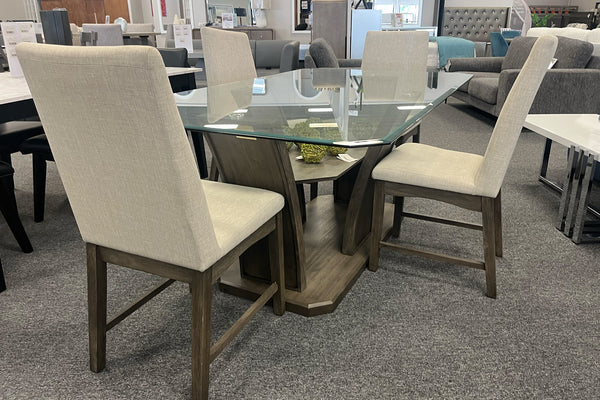 Juego de comedor contemporáneo con mesa rectangular de vidrio templado y base escultórica de madera en tono nogal, acompañado de cuatro sillas tapizadas en color marfil. Exhibido en una tienda de muebles con estilo moderno y elegante.