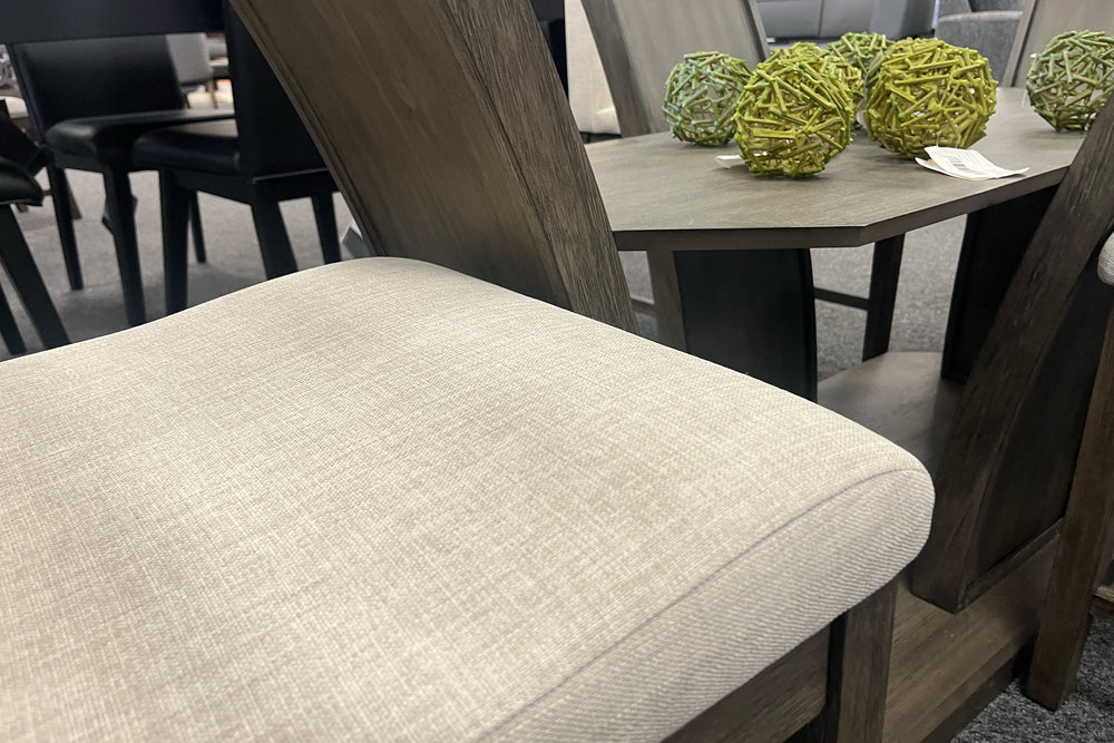 Silla "counter height" con base de madera marrón grisáceo con acolchado crema en un fondo blanco. 