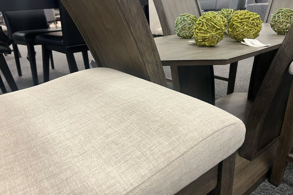 Primer plano de silla de comedor con asiento tapizado en color marfil y estructura de madera oscura, junto a la base decorativa de una mesa con estante inferior. Diseño contemporáneo que combina comodidad, funcionalidad y elegancia.