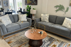 Sala de estar con sofá y loveseat grises, una mesa de centro de madera y elementos decorativos una sala de exposición