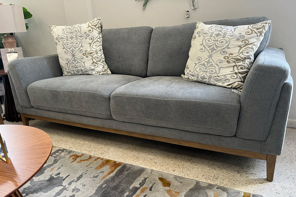 Sofá gris con cojines estampados en un ambiente de sala de exposición
